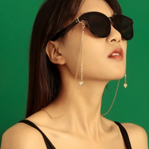 Goldene Brillenkette mit Herzanhänger an einer Sonnenbrille vor grünem Hintergrund