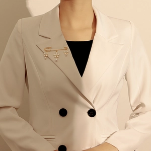 Détail d'une broche épingle dorée avec fleurs blanches et perles sur un blazer
