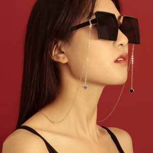 Goldene Brillenkette mit schwarzen Herzanhängern am Model vor rotem Hintergrund