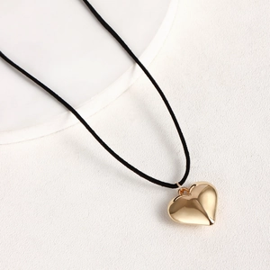 Primer plano de un gran colgante de corazón dorado en un collar de cordón negro