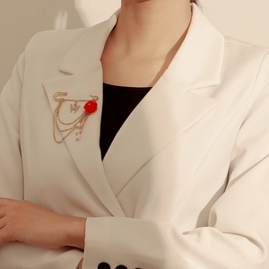 Détail d'une broche vintage dorée avec rose rouge et chaînes sur un blazer blanc