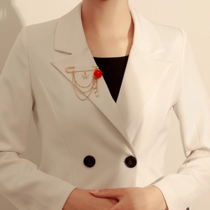 Détail d'une broche dorée avec rose rouge, papillon et chaîne de perles sur un blazer blanc