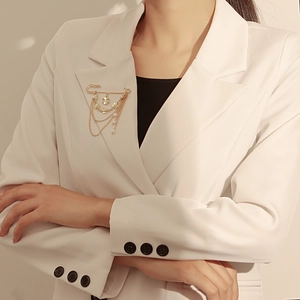 Détail d'une broche chaîne dorée avec perles et pendentif fleur sur un blazer blanc
