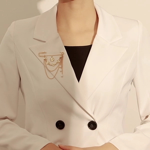 Détail d'une broche à chaîne dorée avec perles portée sur le revers d'un blazer blanc
