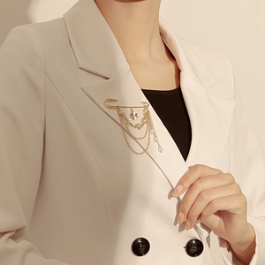 Détail de broche épingle dorée avec chaînes, fleurs blanches et perles sur blazer blanc