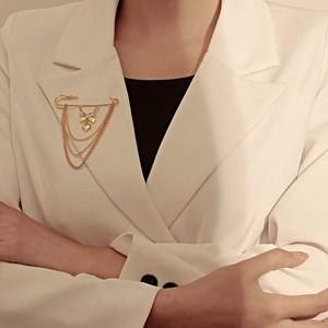 Détail d'une broche épingle dorée avec nœud et pendentifs cœur sur un revers de veste