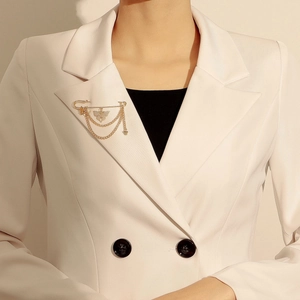 Détail d'une broche papillon dorée avec chaînes sur le revers d'un blazer beige chic