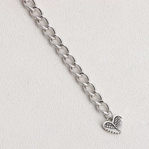 Detailed close-up of a silver chain featuring a heart-shaped pendant with wing texture details