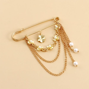 Détails d'une broche épingle à nourrice dorée avec chaînes, perles et pendentif trèfle