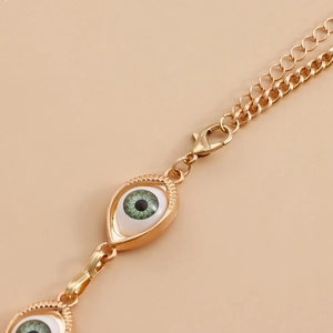 Detailed macro view of the golden metal chain with green evil eye pendants and lobster clasp