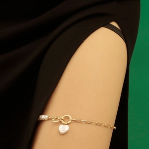 Detailed macro view of golden leg chain featuring white pearls and heart-shaped charm