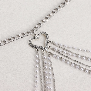 Detail of silver body chain featuring a vintage heart buckle and white pearl tassels