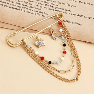Détail d'une broche chaîne vintage dorée avec pendentifs papillon, lune et strass