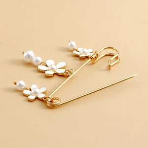 Détail de la broche fleur dorée avec pétales en émail blanc et perles suspendues