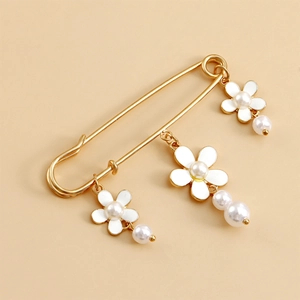 Détail d'une broche épingle dorée avec des fleurs blanches et des perles suspendues