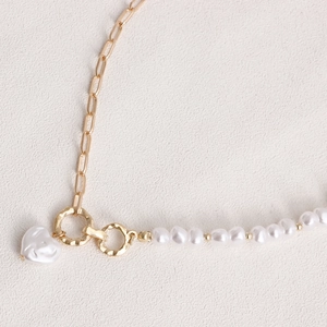 Detailed close-up of a gold link chain and pearl leg strap with heart pendant charm