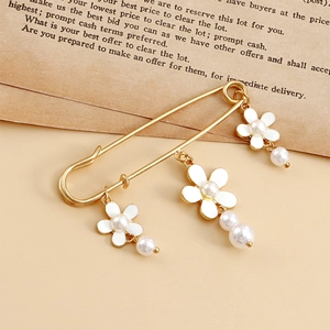 Détail d'une broche épingle dorée vintage avec fleurs en émail et perles blanches suspendues