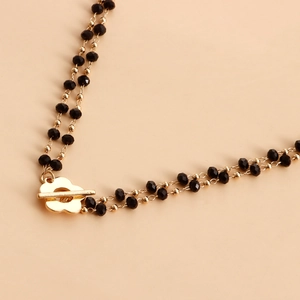 Detailed close-up of double-layer leg chain with gold floral T-bar clasp and black beads