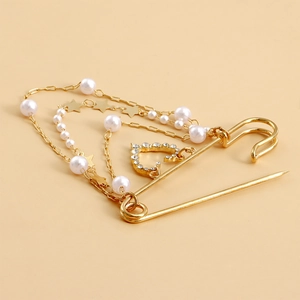 Détail d'une broche épingle dorée avec chaînes multicouches, perles et pendentif cœur