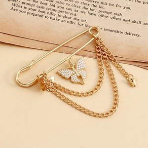 Détail d'une broche épingle vintage dorée avec chaînes et papillon en perles
