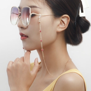 Detail of bohemian gold eyewear chain with red evil eye beads worn by a model