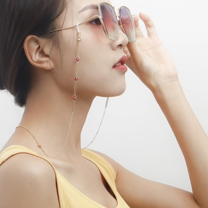 Close-up of golden metal eyeglass chain with red devil eye charms on a model