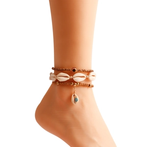 Detail view of bohemian shell and evil eye anklet set on female model with white background