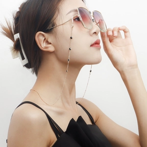 Détail d'une chaîne de masque dorée avec perles noires portée par un mannequin chic