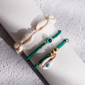 Detail of bohemian shell and green beaded anklet set with an evil eye charm on white display