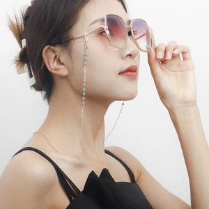 Détail d'une chaîne de lunettes dorée avec perles bleu ciel sur de grandes lunettes