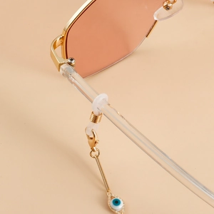 Detail view of colorful evil eye pendant on golden metal eyewear chain and sunglasses