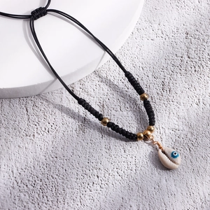 Detail of bohemian black woven cord anklet with natural shell and evil eye charm