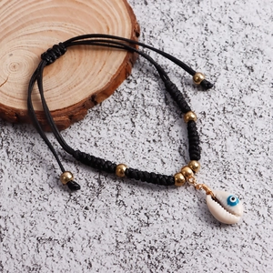 Detail of bohemian woven anklet featuring cowrie shell and blue evil eye charm