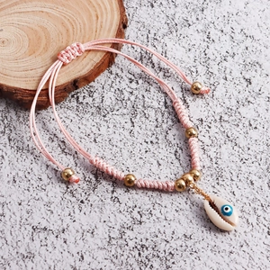Detail of pink woven anklet with shell charm and evil eye bead on wooden slice