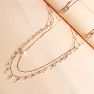 Détail d'un collier doré à trois rangs avec strass, petits disques et une perle blanche