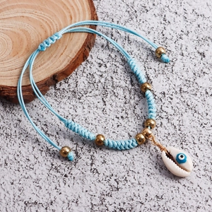 Close-up of Bohemian woven anklet with blue evil eye shell charm and golden beads