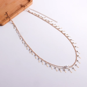 Détail d'une chaîne de corps dorée ornée de perles et de pendentifs strass en gouttes