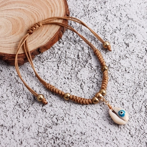Detail view of handmade bohemian cord anklet with shell pendant and evil eye pattern
