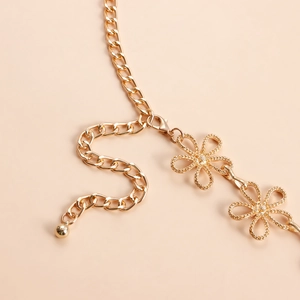 Détail macro de la chaîne de taille en métal doré avec pendentifs fleurs et fermoir