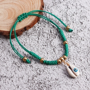 Detail of handmade green woven anklet with shell charm and evil eye bead on wood