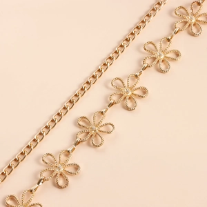 Détail macro d'une ceinture chaîne en métal doré avec motifs floraux creux et fini poli