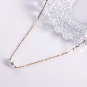 Détail d'une chaîne de corps minimaliste dorée avec une perle blanche d'imitation élégante