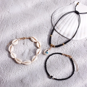 Bohemian 3-piece set with shell and evil eye beads on light sandy beach background