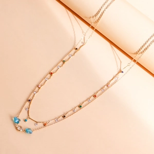 Detail of a gold double-layer chain with colorful beads and a blue gemstone drop pendant