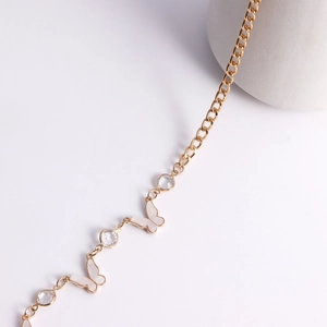Detail of gold metal waist chain featuring white enamel butterfly and sparkling crystals