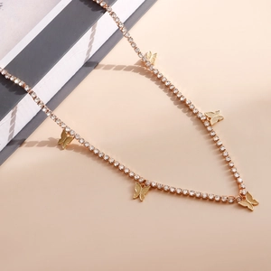 Dettaglio della collana a catena dorata con strass e cinque ciondoli a farfalla su beige