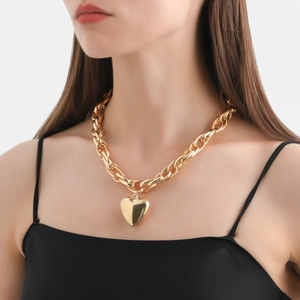 Close-up of chunky gold hollow oval link chain with a polished large heart pendant on a model