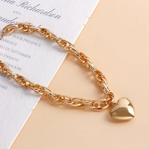 Close-up of golden chunky chain necklace with a polished 3D heart pendant on elegant paper