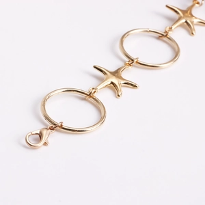 Macro detail of golden starfish and ring link chain with lobster clasp closure