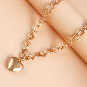 Detail of chunky gold chain necklace with polished heart pendant on beige stand